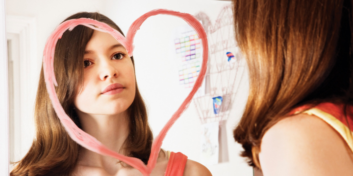 Girl looking at reflection in mirror decorated with heart-shape