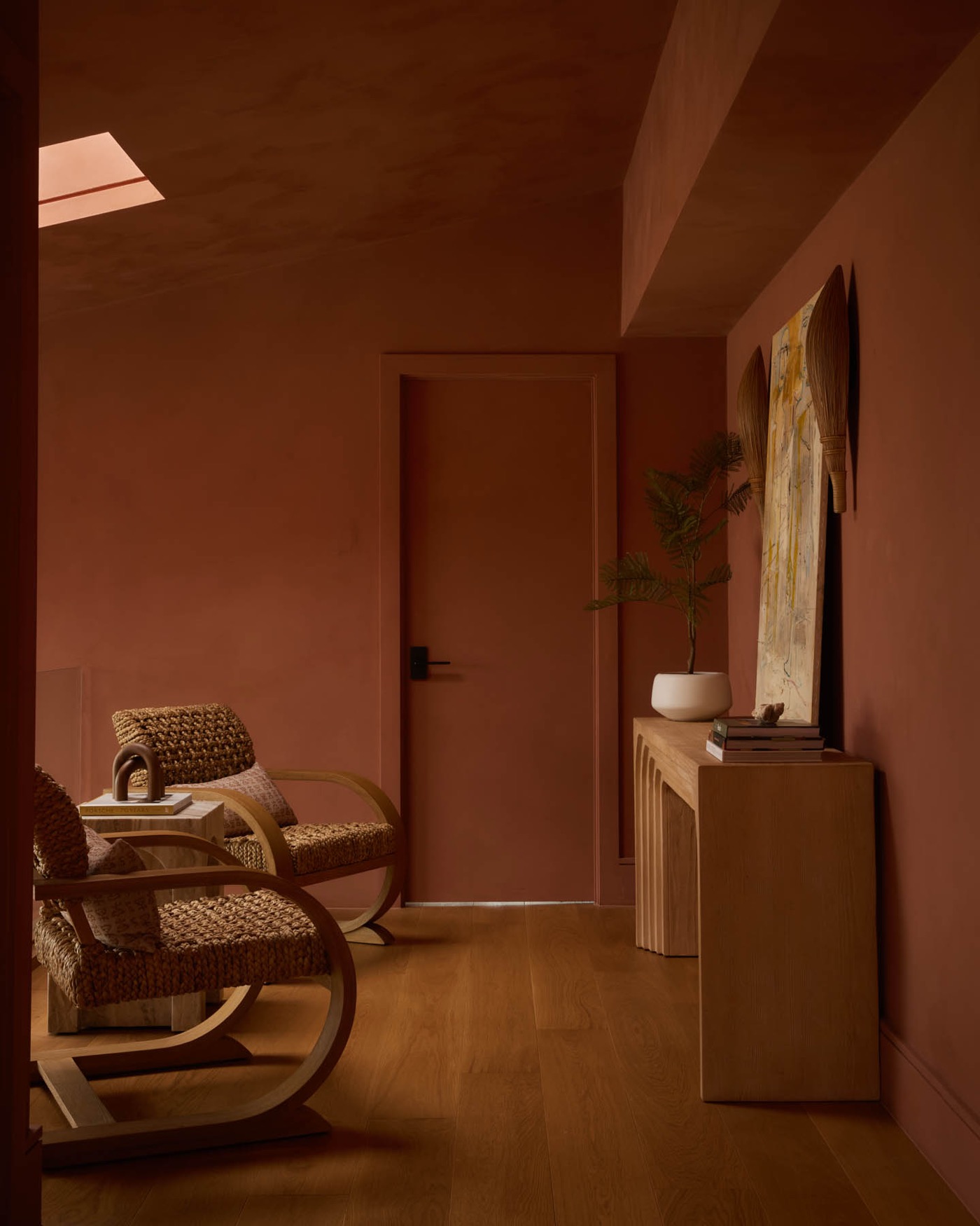 Không gian tường màu terracotta với ghế đan thủ công và sàn gỗ sáng